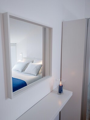 Una camera moderna con un ampio specchio, un comodino e un letto con biancheria bianca.