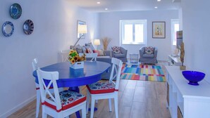 A modern living room with a round dining table, white chairs, a colorful rug, and a blue bowl on a white table. - Grandchildren's House (Mafra)