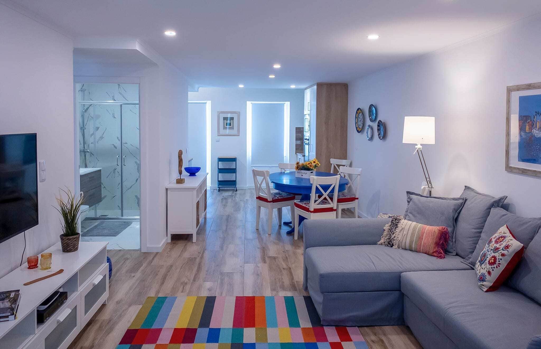 A modern living room with a grey sofa, a flat-screen TV, and a colorful rug.