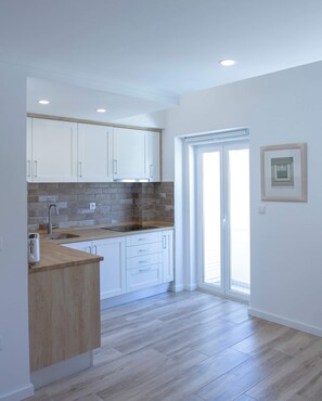 A modern kitchen with white cabinets, a brick backsplash, and a wooden countertop.