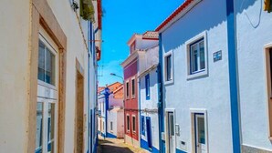 A narrow cobblestone street flanked by colorful buildings with multiple windows and doors.