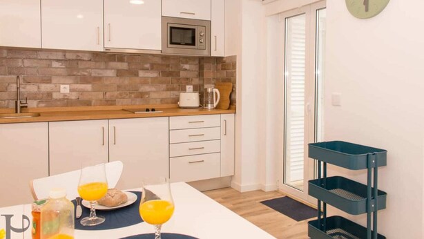 A modern kitchen with white cabinets, a microwave, and a brick backsplash.