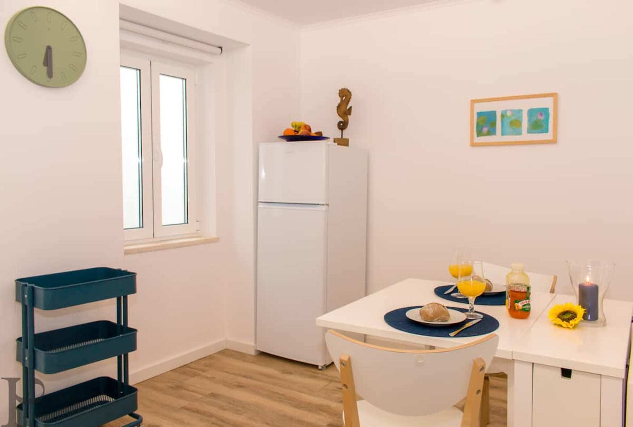 Una cucina compatta con un frigorifero, un tavolo da pranzo con un sottopiattino blu e una sveglia a parete.