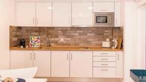A modern kitchen with white cabinets, a microwave, and a brick backsplash.