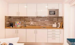 Una cucina moderna con mobili bianchi, un forno a microonde e uno schienale in mattoni.