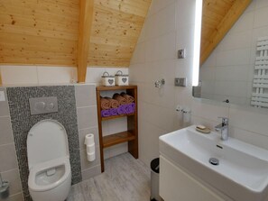 A modern bathroom with a toilet, a sink, and a mirror. There are towels and toiletries on shelves. - Beautiful Pondside Villa (Korenov)