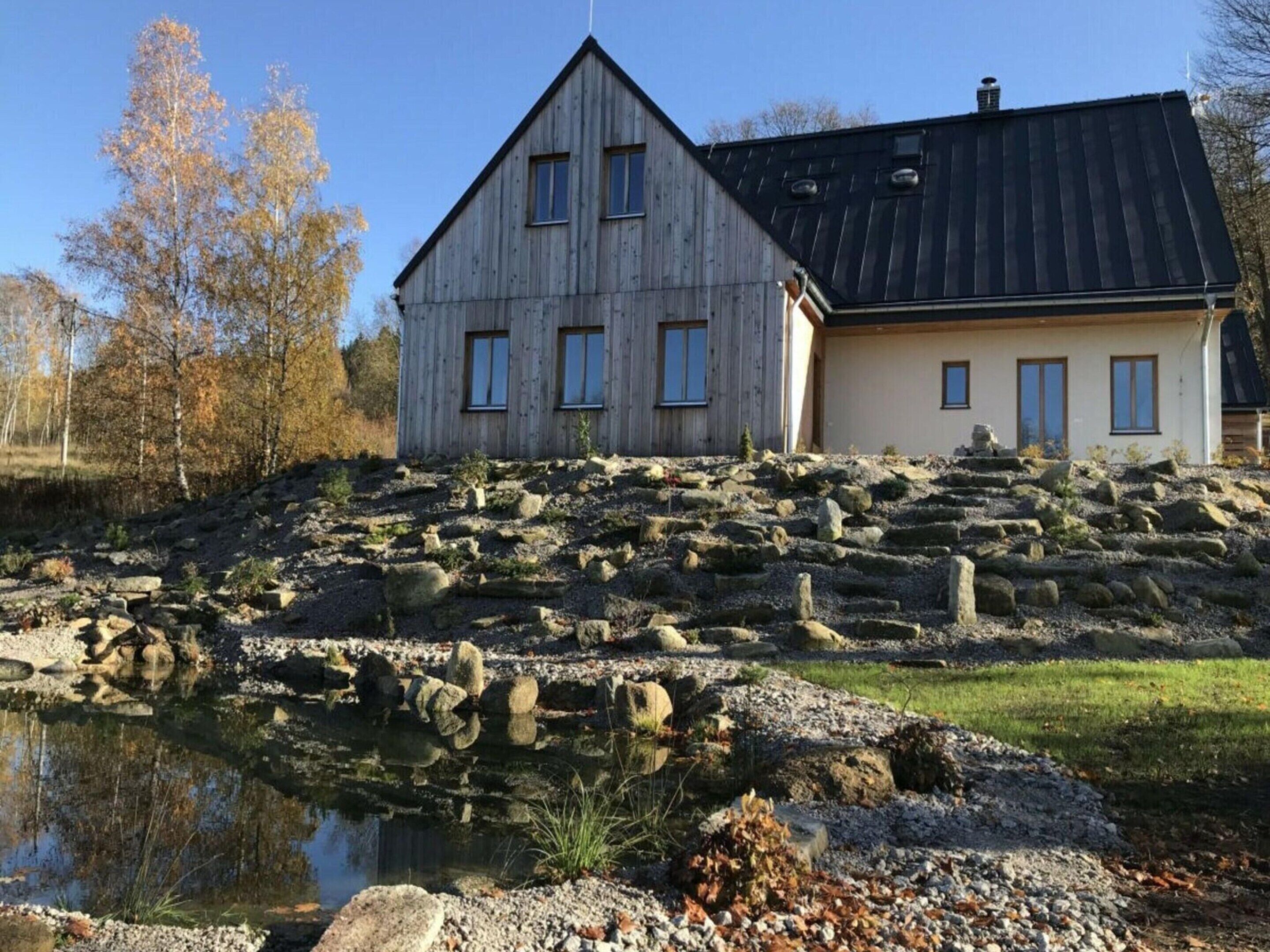 A rustic wooden house with a stone pathway leading to a pond.