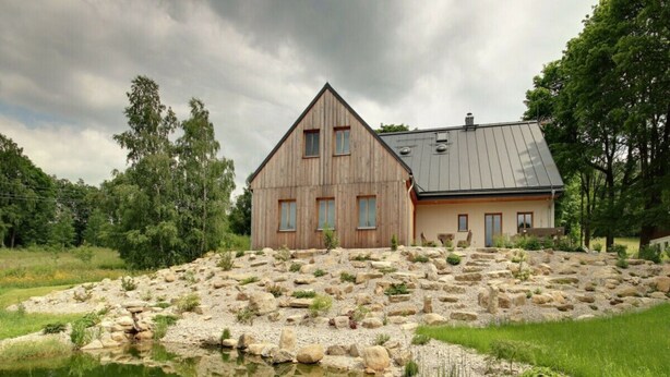 A wooden house with a sloped roof, a pond in front, and a rocky garden area. - Beautiful Pondside Villa (Korenov)