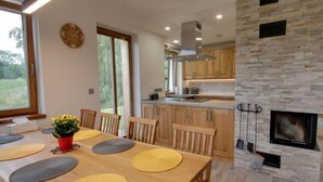 A modern kitchen with wooden cabinets, a stone fireplace, and a dining area with a wooden table and chairs. - Beautiful Pondside Villa (Korenov)