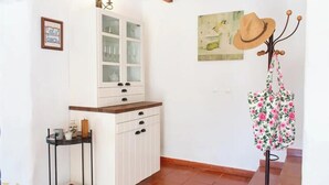 Een kamer met een wit kastje, een kleine tafel met spullen, een hoed op een standaard en een schilderij aan de muur.