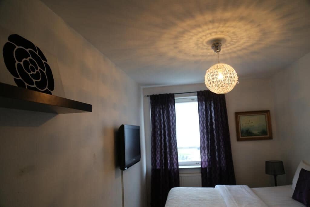 Hotelkamer met een bed, een flatscreen televisie, een kroonluchter, een raam met gordijnen en een schilderij aan de muur.