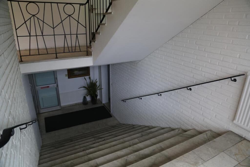 A staircase with a metal handrail, white brick walls, and a door at the bottom.