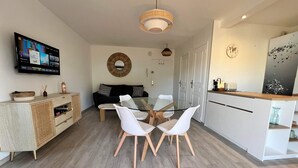 A modern kitchen with a dining area, a TV mounted on the wall, and a round mirror above the sofa.