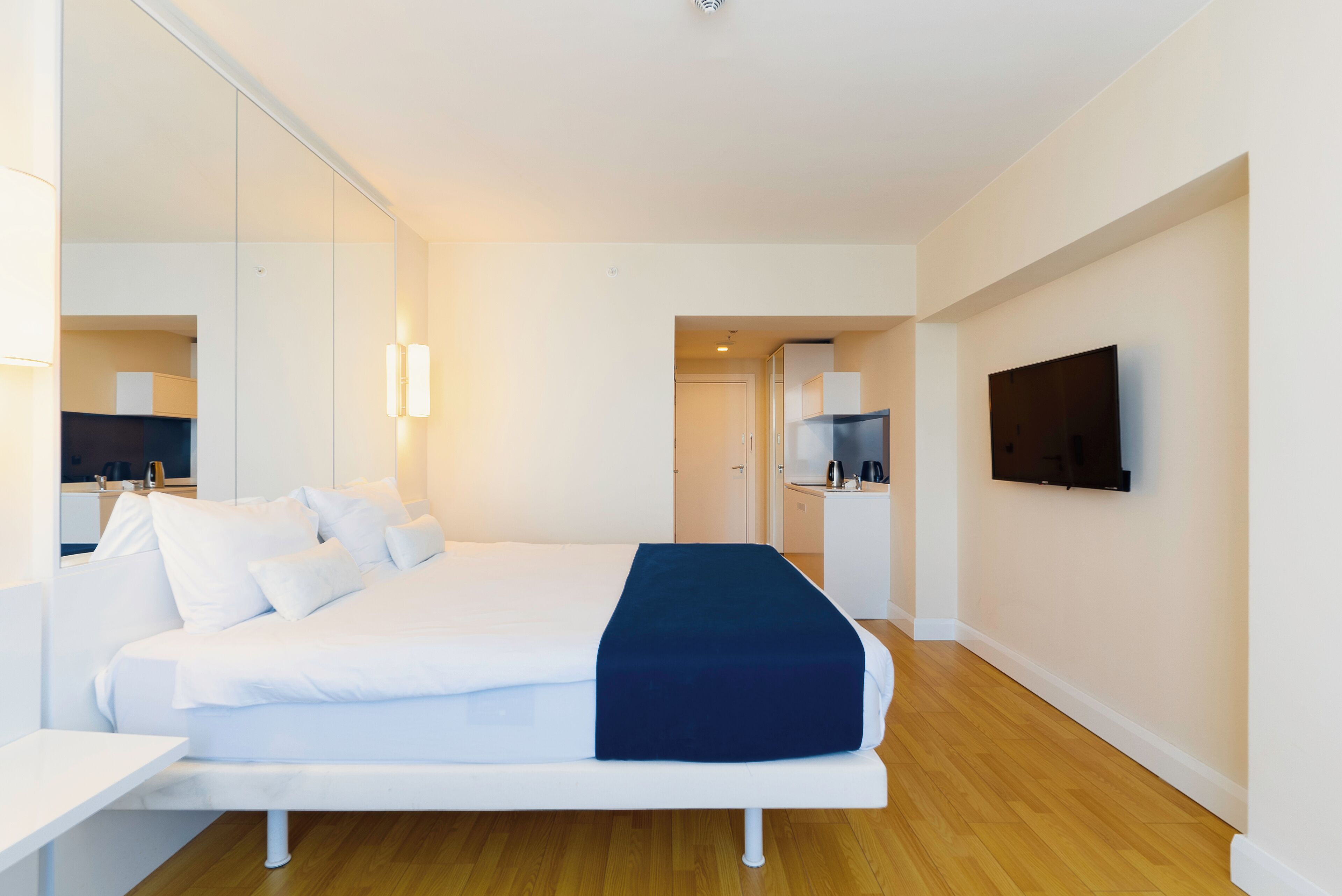 Una habitación de hotel moderna con una cama grande, un televisor de pantalla plana y una pequeña kitchenette.