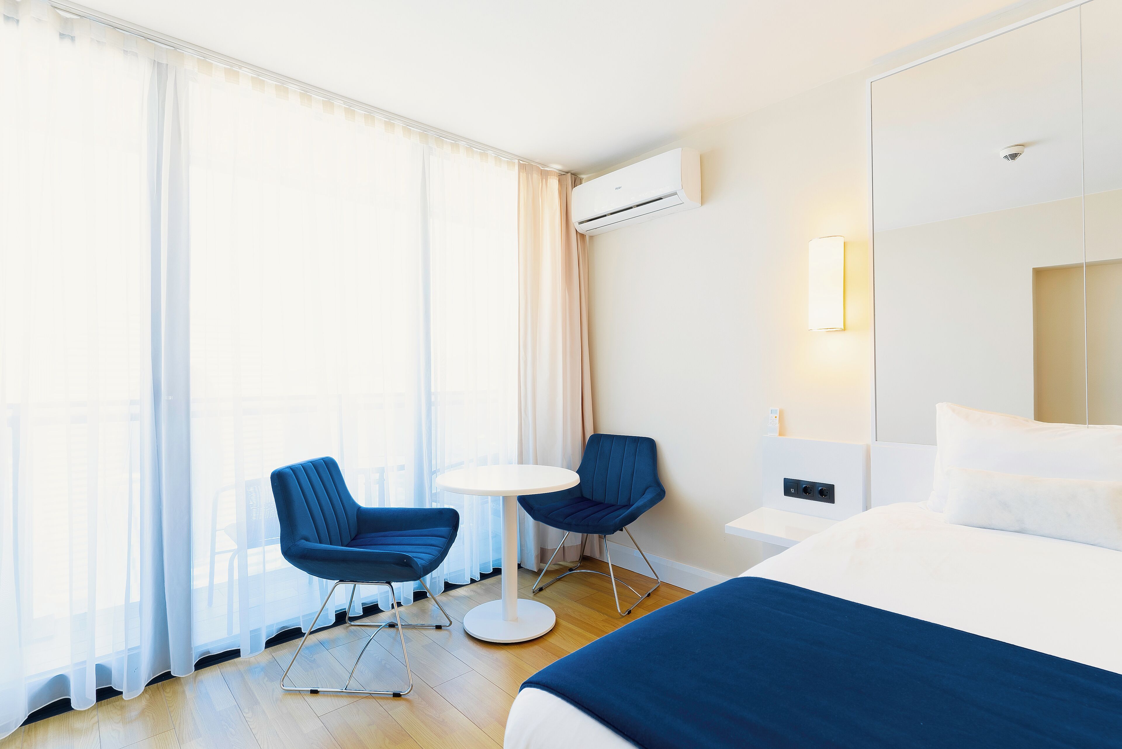 Una habitación de hotel con una cama, dos sillas, una mesita y un ventanal con cortinas.