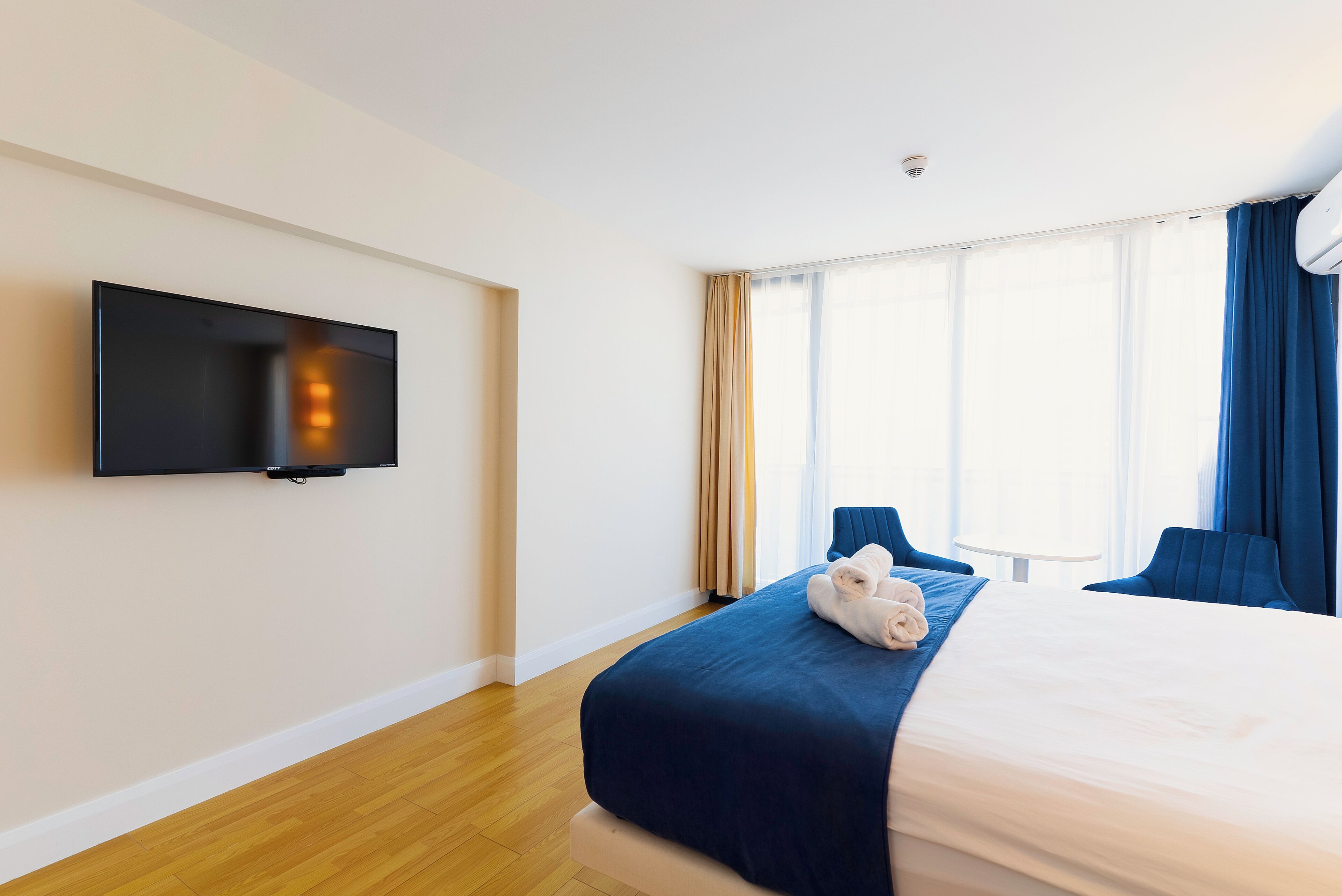 Habitación de hotel con cama, televisión de pantalla plana en la pared y un amplio ventanal con cortinas.