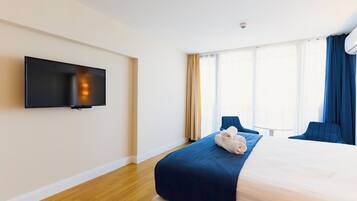 Habitación de hotel con cama, televisión de pantalla plana en la pared y un amplio ventanal con cortinas.