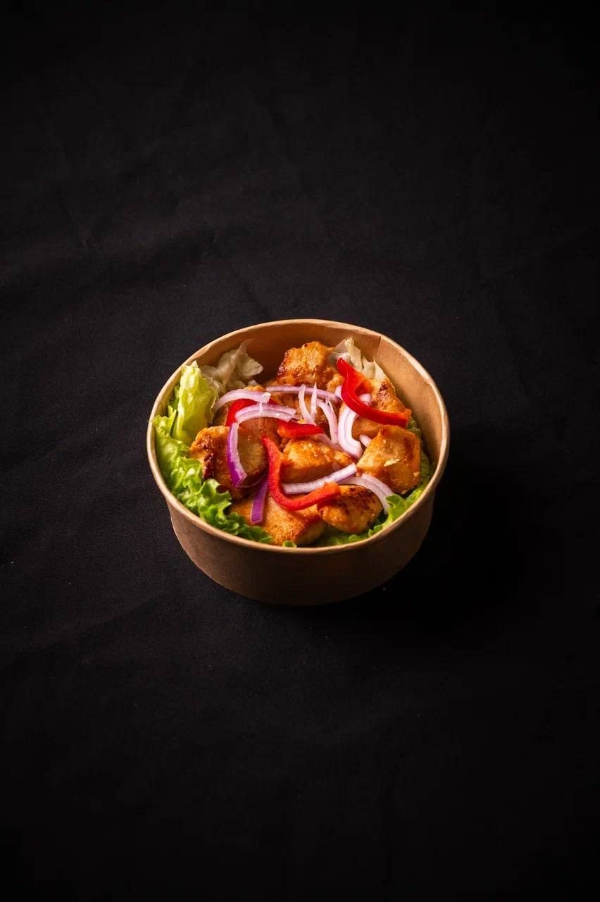 A bowl of food with lettuce, red onions, and red bell peppers on a dark background.