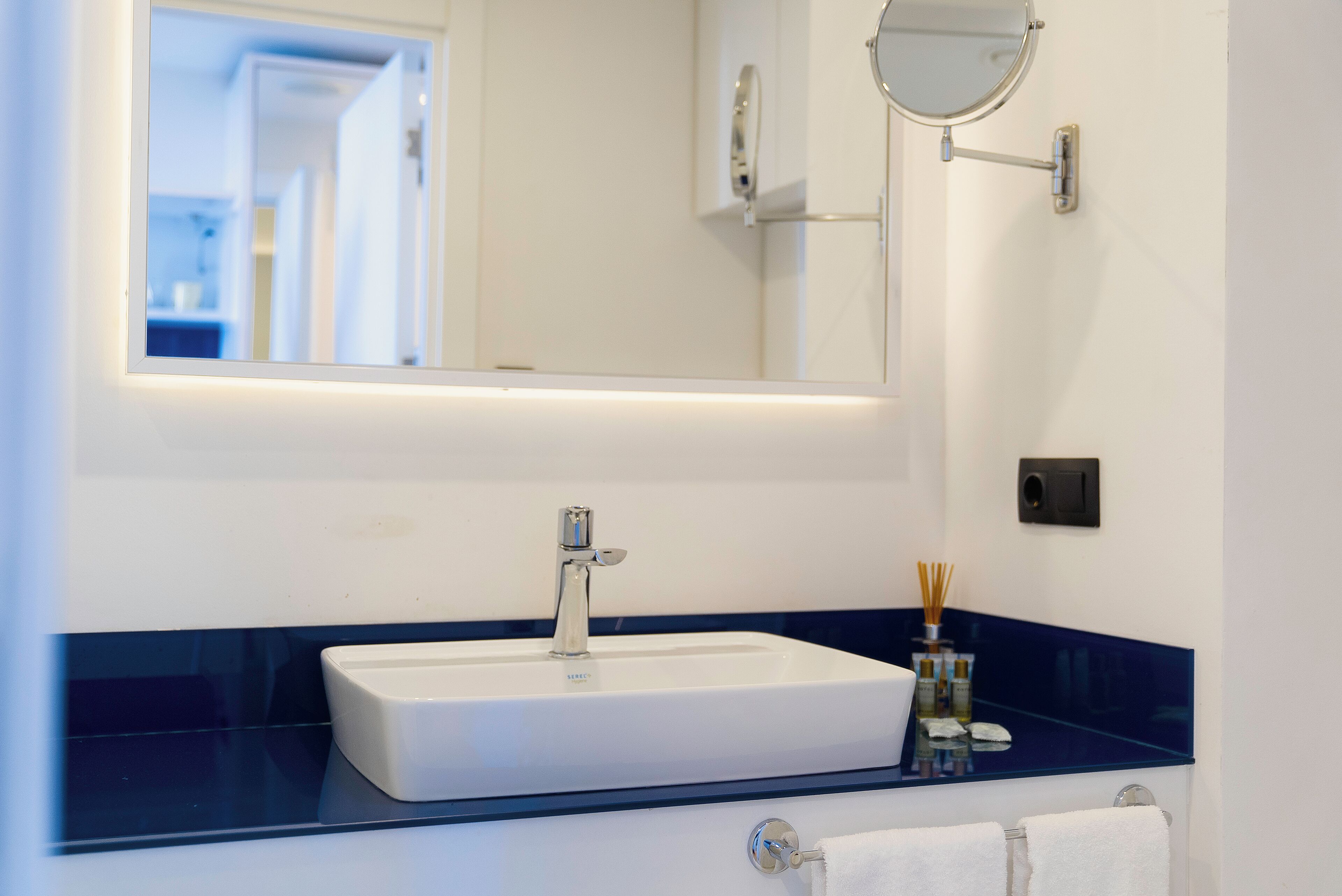 A bathroom with a white sink, a blue countertop, a mirror, and a towel rack.