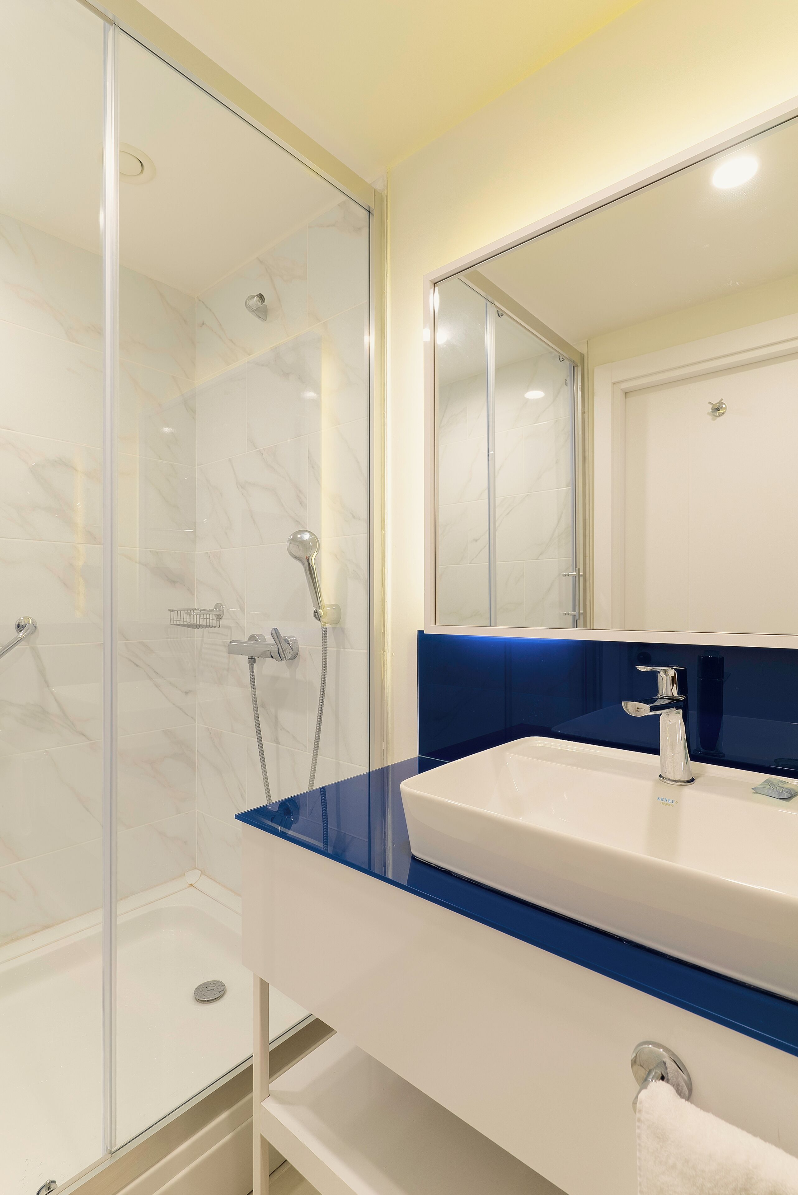 A modern bathroom with a glass-enclosed shower, a white sink with a blue countertop, and a large mirror above the sink.
