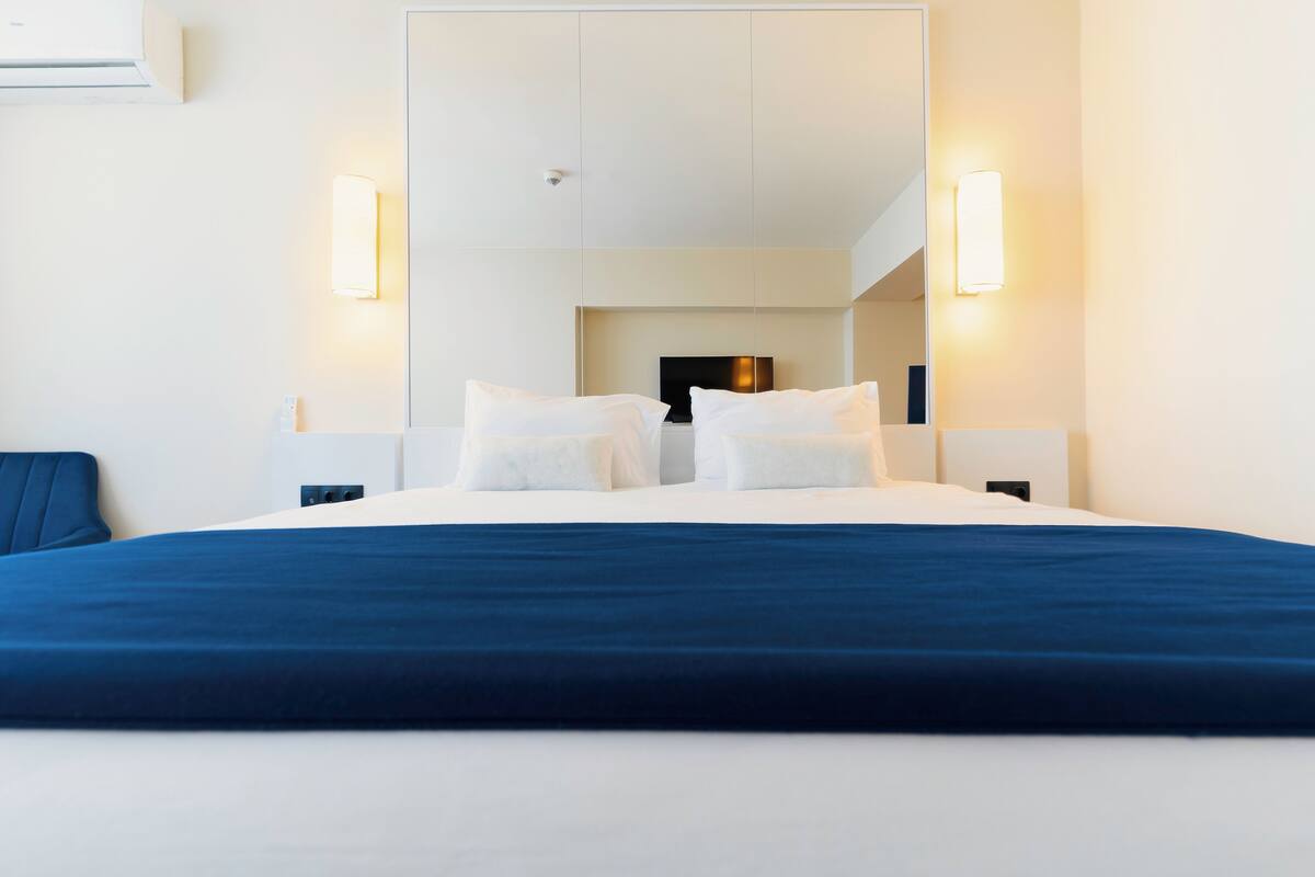 Una habitación de hotel moderna con una cama grande, dos mesitas de noche, un televisor de pantalla plana y apliques de pared.