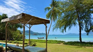 A wooden gazebo with a mattress, a pool, and a view of the sea and mountains.