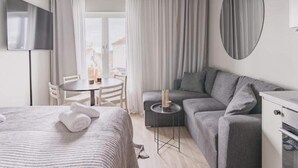 Ein modernes Hotelzimmer mit Bett, Sofa, kleinem Tisch mit Kerze, Fernseher und Blick ins Freie.