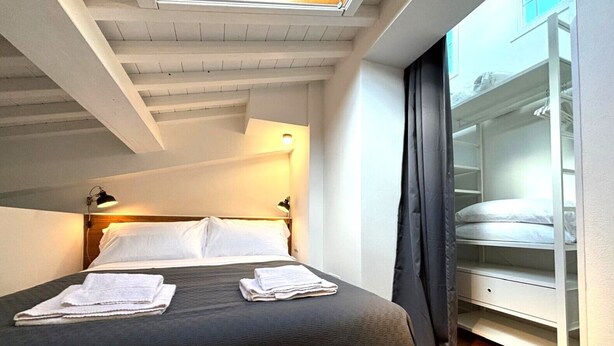 A bedroom with a bed, two bedside lamps, a skylight, a wardrobe, and a window with curtains.