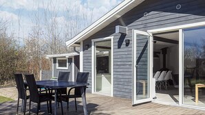 Una casa moderna con una terraza, un comedor con sillas y un amplio ventanal corredera que da a un espacio exterior.