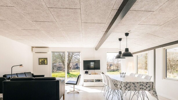 Una sala de estar moderna con un sofá negro, una mesa de comedor con sillas, un televisor y un ventanal con vistas al exterior.