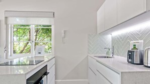 Una cocina moderna con horno integrado, ventana con vista a follaje, salpicadero con patrón de espiga y encimera con tostadora y hervidor.