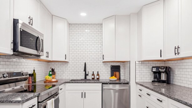 Cozinha moderna com armários brancos, eletrodomésticos de aço inoxidável e painel de azulejos.