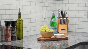 Uma bancada de cozinha com uma tigela de uvas verdes, uma garrafa de água gaseificada S. Pellegrino, um bloco de facas de madeira e vários recipientes de temperos.