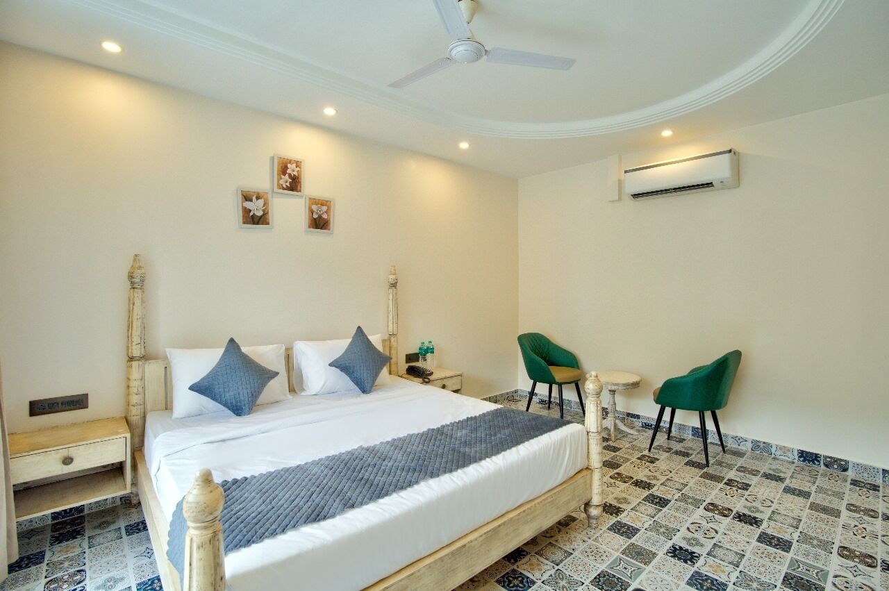 A hotel room with a bed, two chairs, an air conditioning unit, and a ceiling fan.