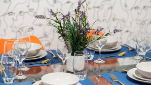 A dining table set with clear glassware, plates, and cutlery, with a decorative plant centerpiece.