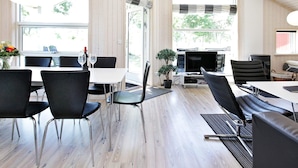 A spacious room with large windows, a dining area with tables and chairs, a seating area with sofas, and a small plant. - 5 Star Holiday Home in Grossenbrode (Grossenbrode)