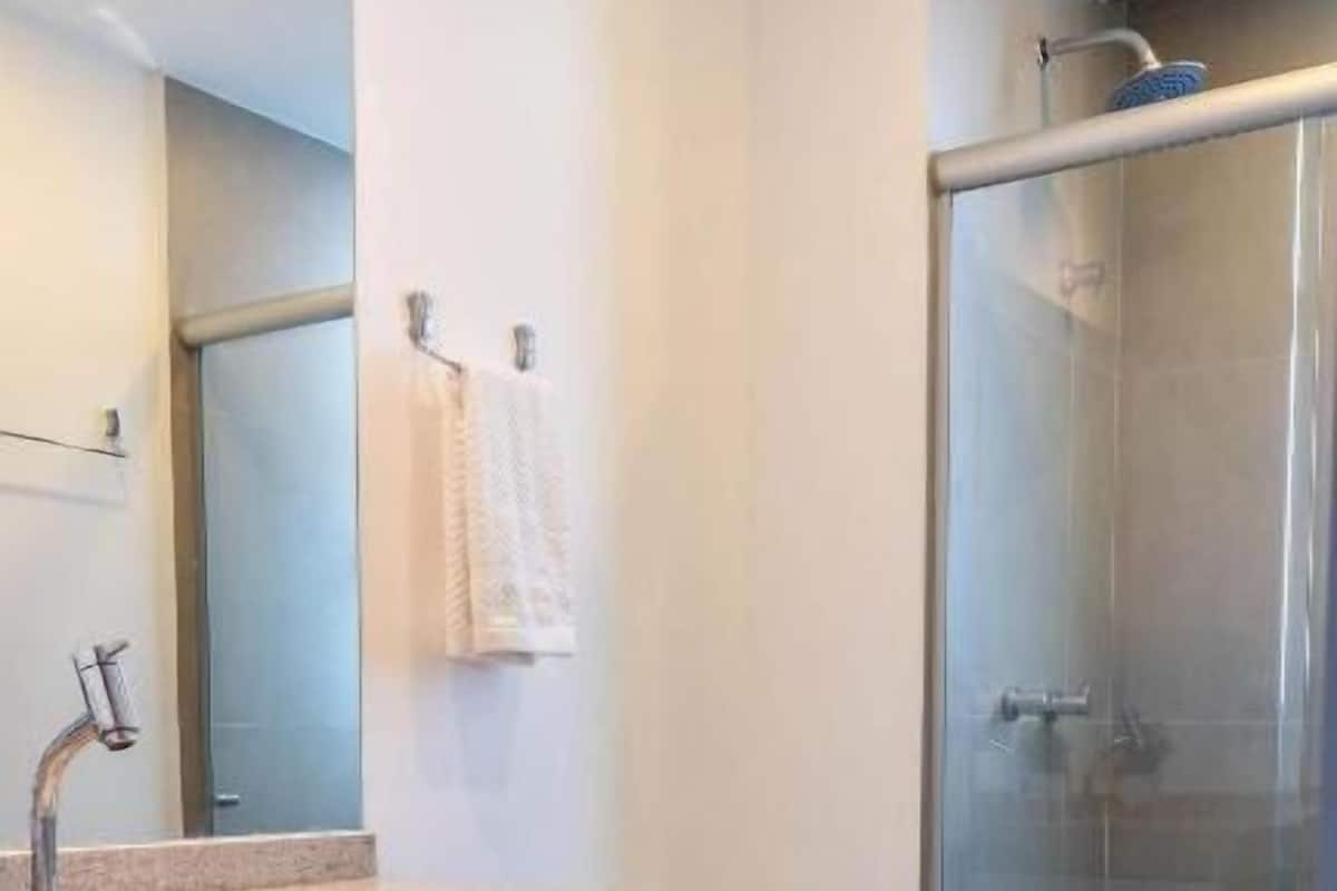 A modern bathroom with a granite countertop, a large mirror, a toilet, and a glass-enclosed shower.