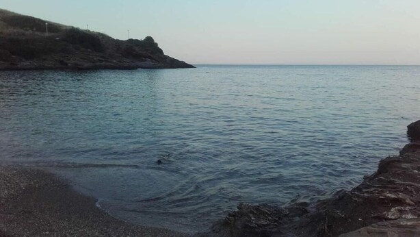 A calm sea with a rocky shoreline and a distant landmass. - Egli's boutique (Lavreotiki)
