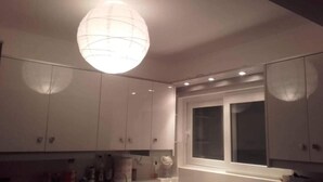 A room with white cabinets, a large window, and a hanging light fixture. - Egli's boutique (Lavreotiki)