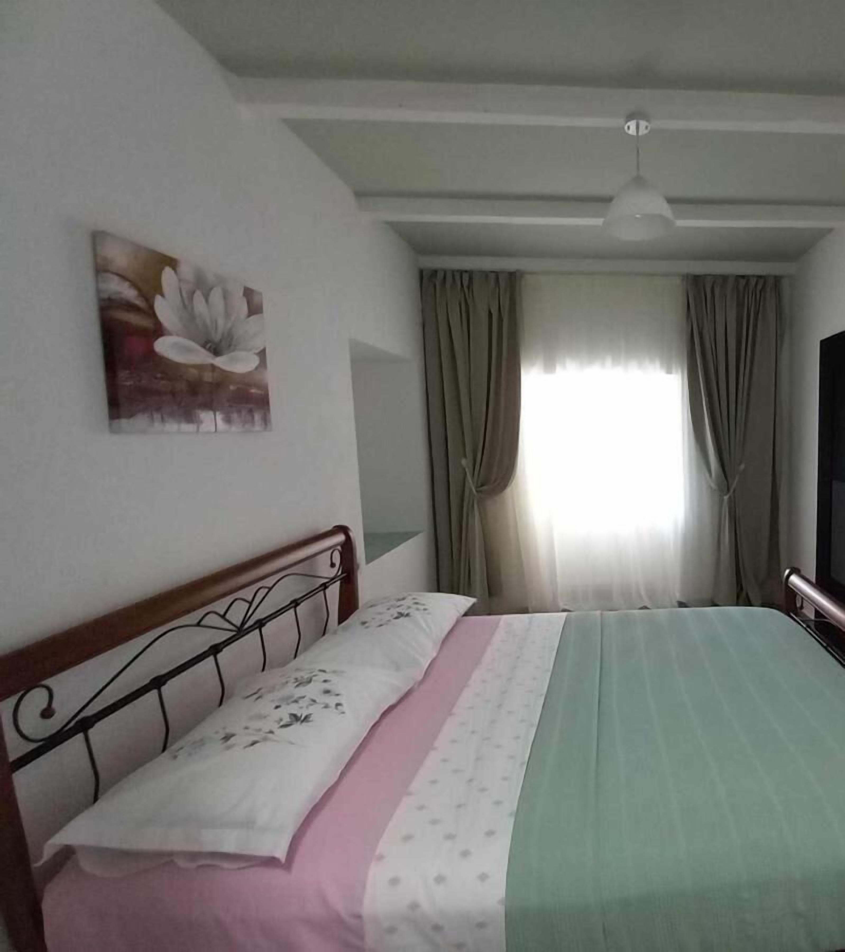 A bedroom with a bed, a painting, a ceiling fan, and a window with curtains.