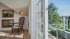 Um quarto com piso de madeira, uma cadeira, uma mesa e duas pinturas emolduradas na parede.