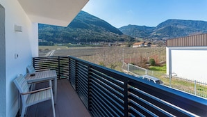 Een balkon met uitzicht op een bergachtig landschap, een tafel en stoelen.