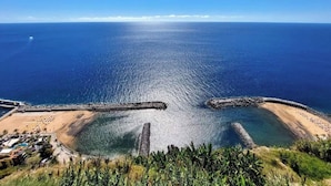 A coastal area with a clear view of the sea, a sandy beach, and a rocky breakwater. - VIEWPOINT HOUSE (Calheta)