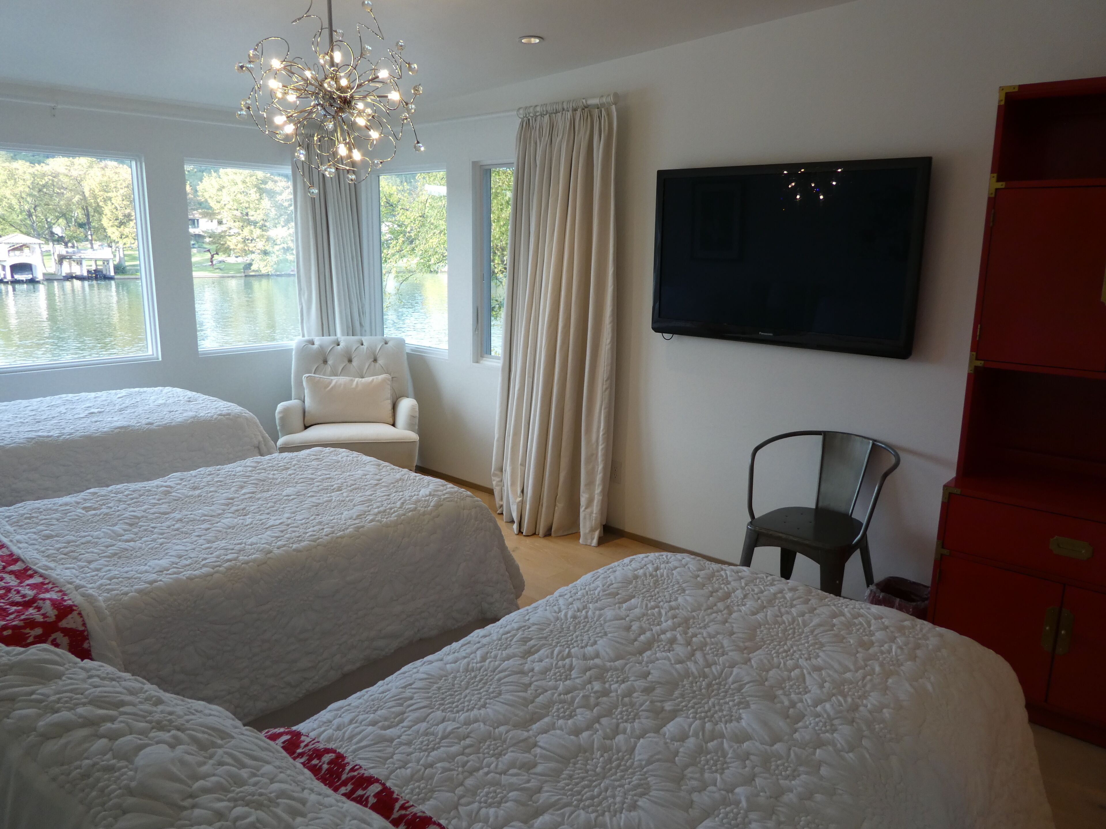 A hotel room with two beds, a TV, a chair, and a view of a lake.