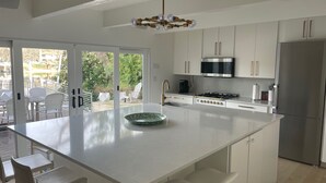 A modern kitchen with white cabinetry, a central island, stainless steel appliances, and a view to an outdoor patio area. - Peaceful Lake Retreat: Modern Luxury, Comfort, Scenic Views & Paddle Boards (Austin)