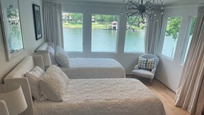 A bedroom with two beds, a chair, and large windows overlooking a lake. - Peaceful Lake Retreat: Modern Luxury, Comfort, Scenic Views & Paddle Boards (Austin)