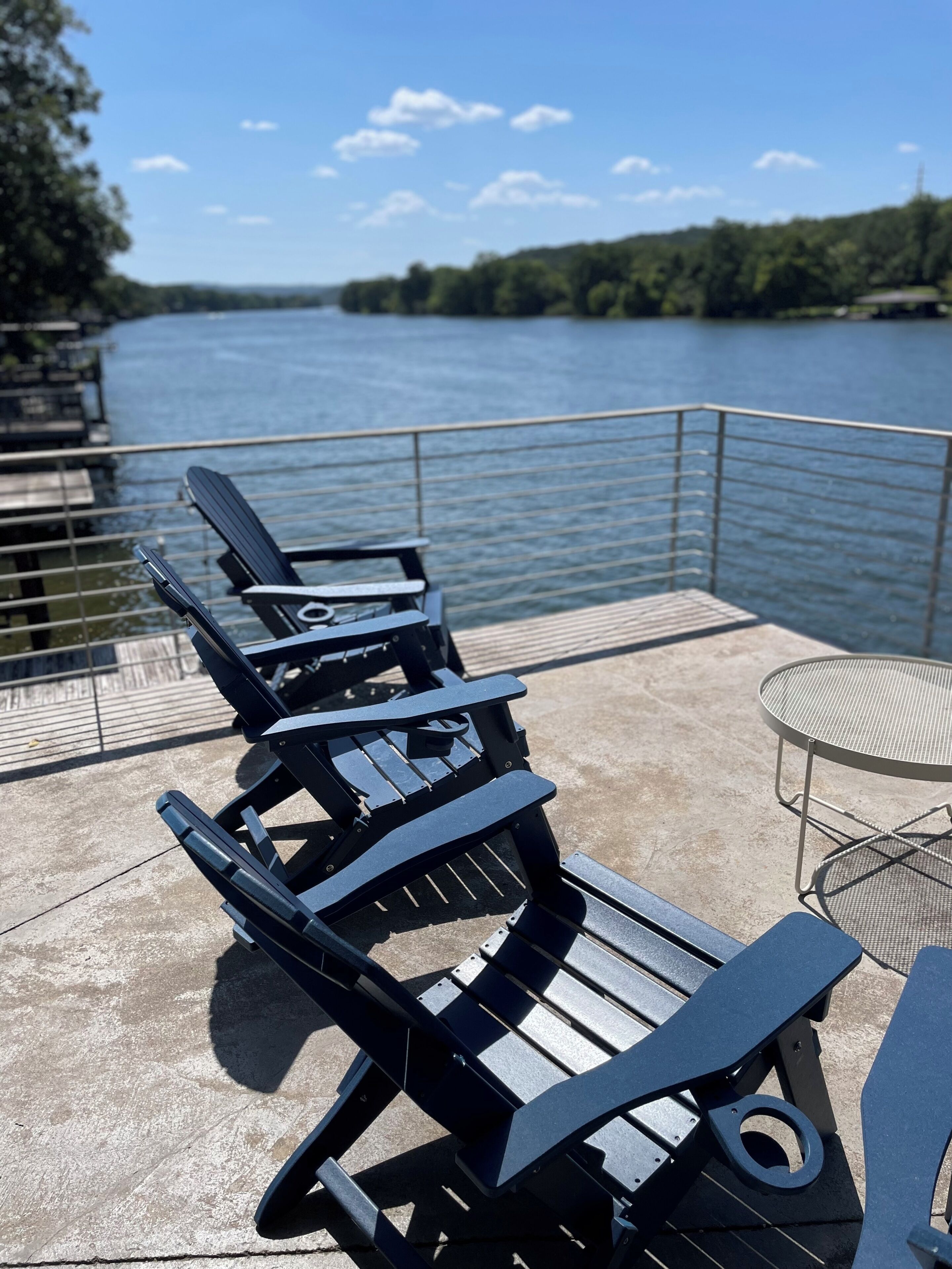 Sillones de exterior con una mesa metálica y barandilla de metal con vista al agua.