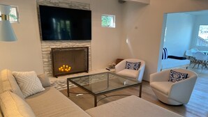 A modern living room with a stone fireplace, a flat-screen TV, and a glass coffee table. - Peaceful Lake Retreat: Modern Luxury, Comfort, Scenic Views & Paddle Boards (Austin)