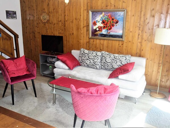 A living room with a white sofa, two pink chairs, a TV, and a painting on the wall.