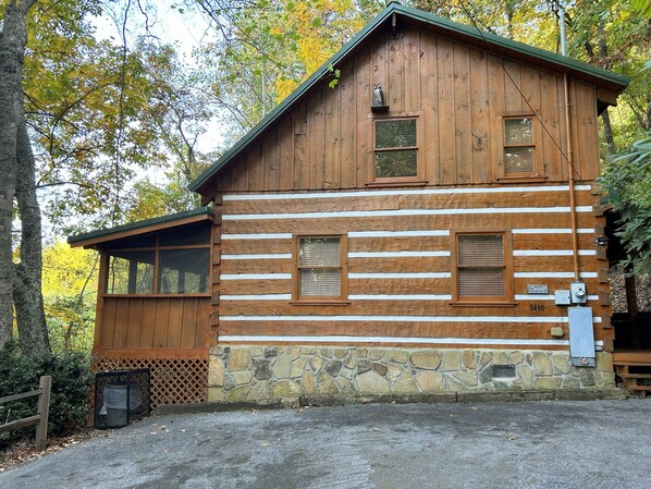 A rustic log cabin with a stone foundation, large windows, and a wooden porch.